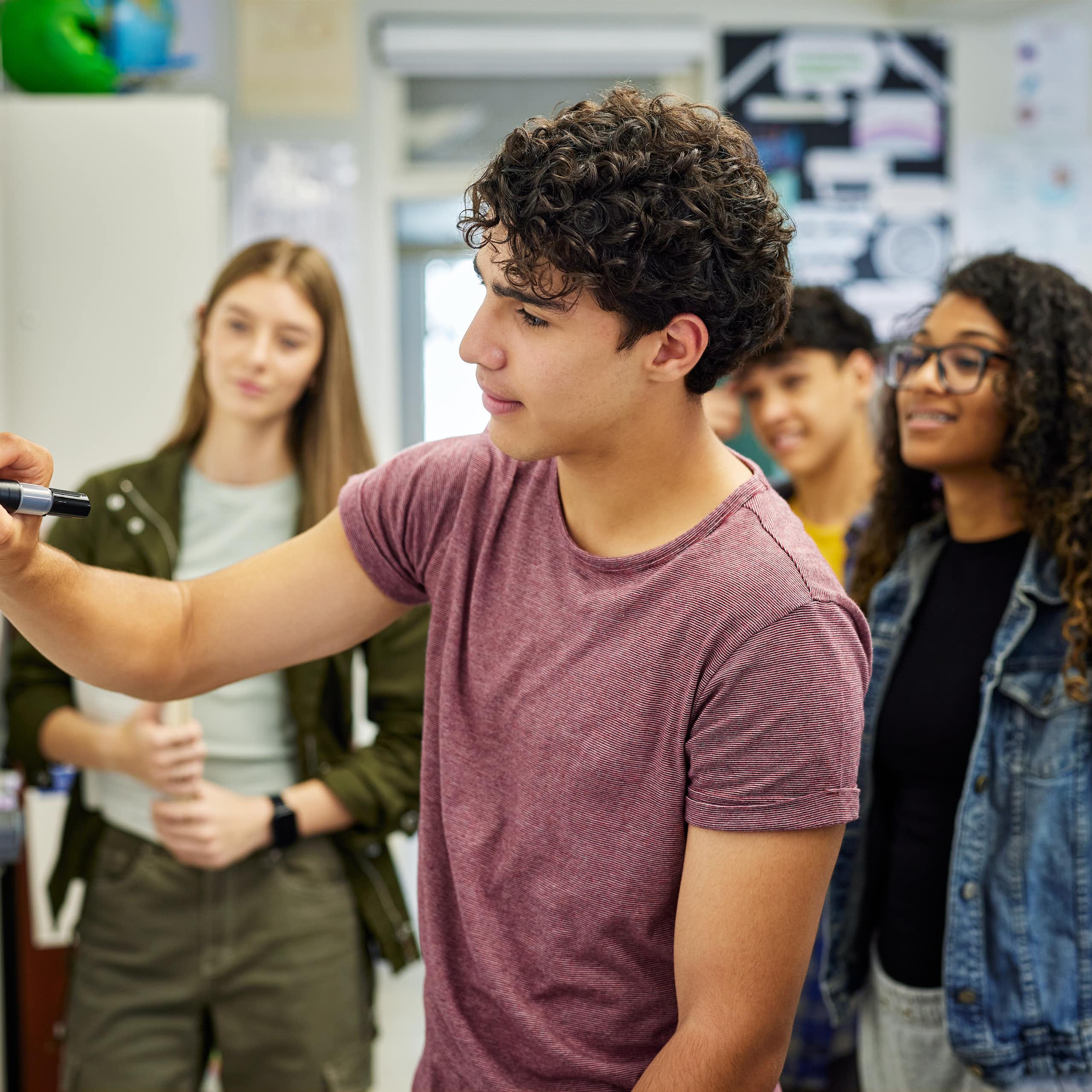 Un chico escribe en una pizarra mientras le observan sus compañeros.