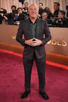 Un hombre con traje sonríe ampliamente mientras los fotógrafos están detrás.