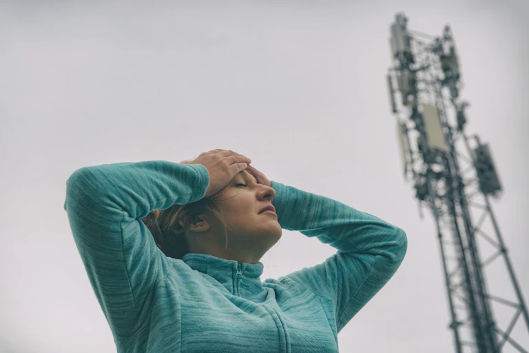 Une femme se tient la tête à proximité d’une antenne-relais.