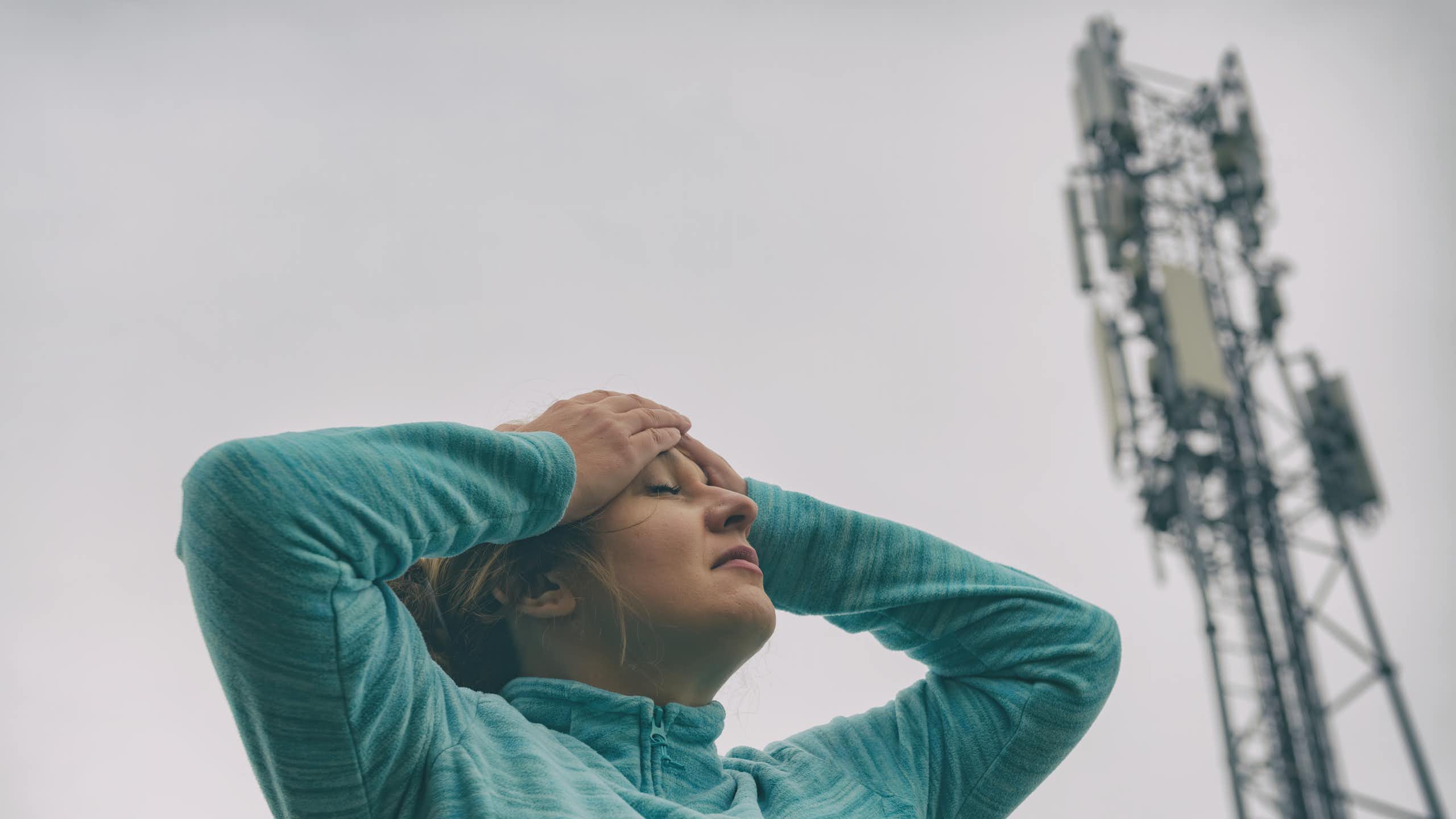 Une femme se tient la tête à proximité d’une antenne-relais.