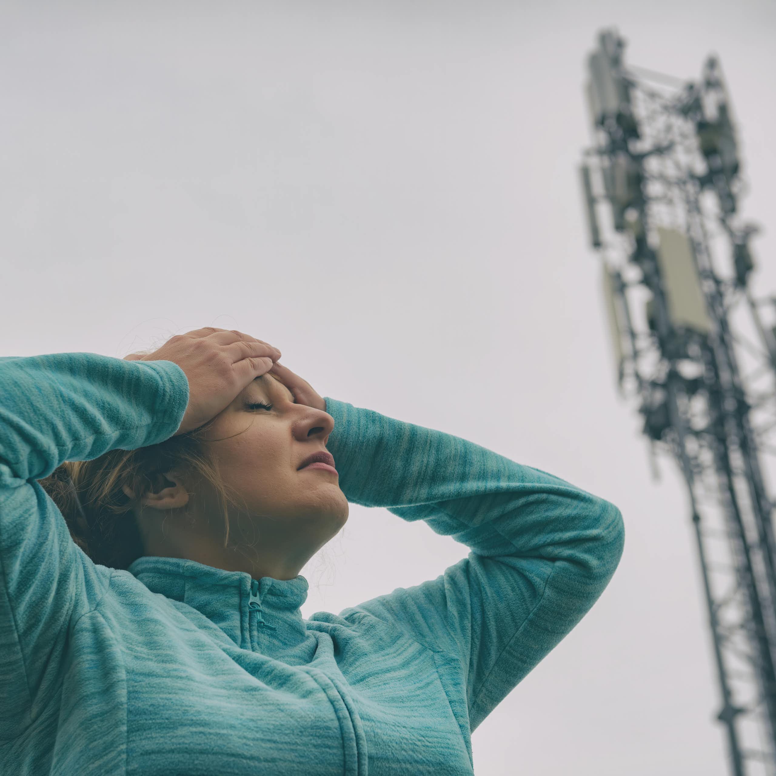 Une femme se tient la tête à proximité d’une antenne-relais.