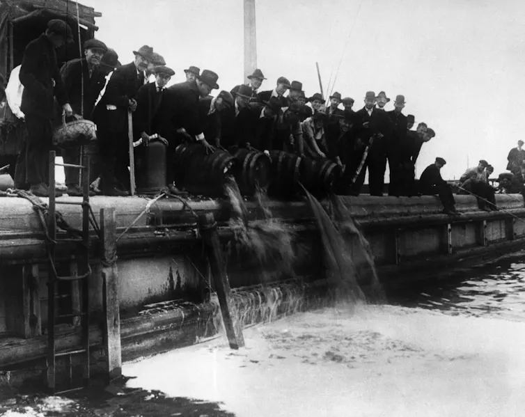 Several men dump beer from kegs into a lake.