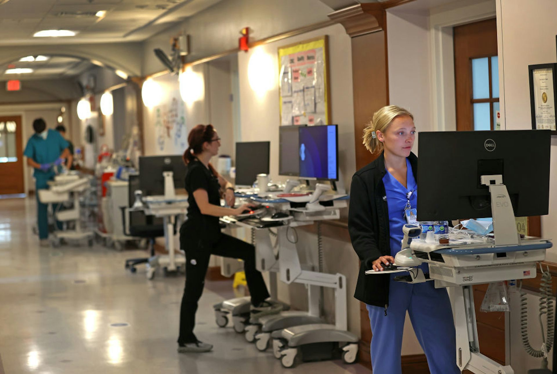 Three nurses work on patient charts outside patient rooms in a hospital.