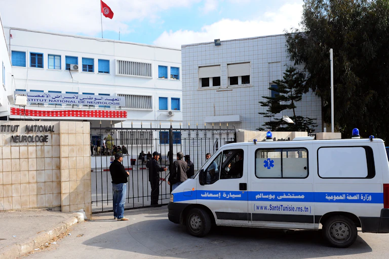 An ambulance at a gate in front of a building which has a flag flying from the rooftop
