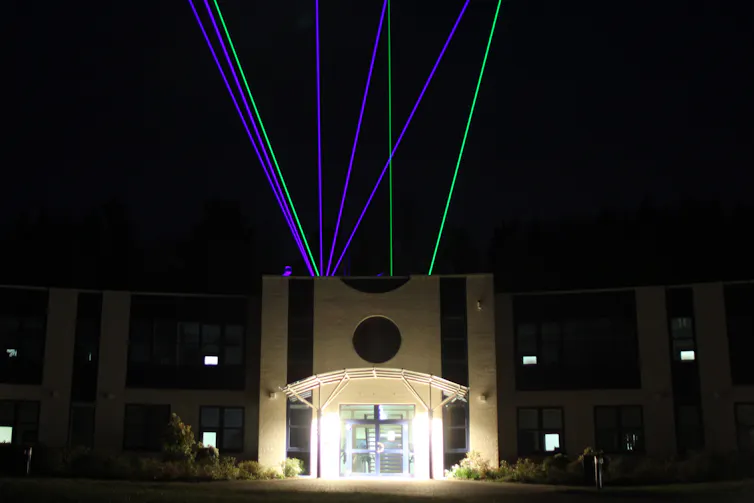 Blue and green lasers shining out of the roof of a large building.