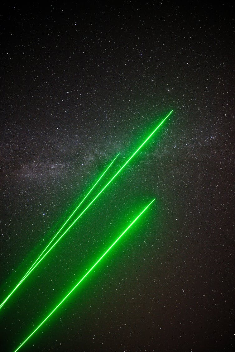 Three green laser beams, with the Milky Way in the background.