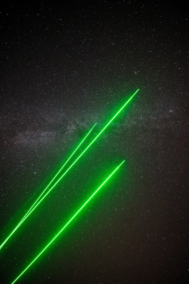 Three green laser beams, with the Milky Way in the background.