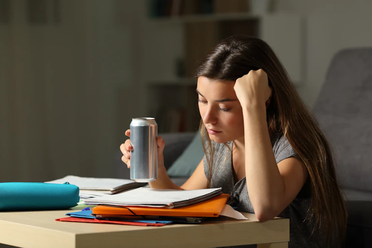 A teen girl studying her notes holds a can of sugary drink on her hand.