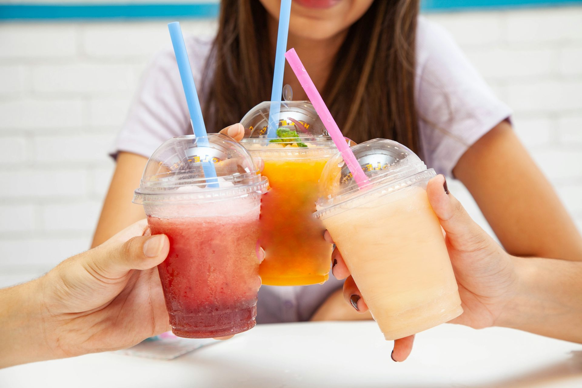 A group of three teens cheers their sugary iced drinks.