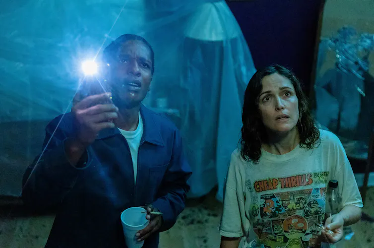 A$AP Rocky and Rose Byrne looking at the ceiling, he is holding up his phone torch