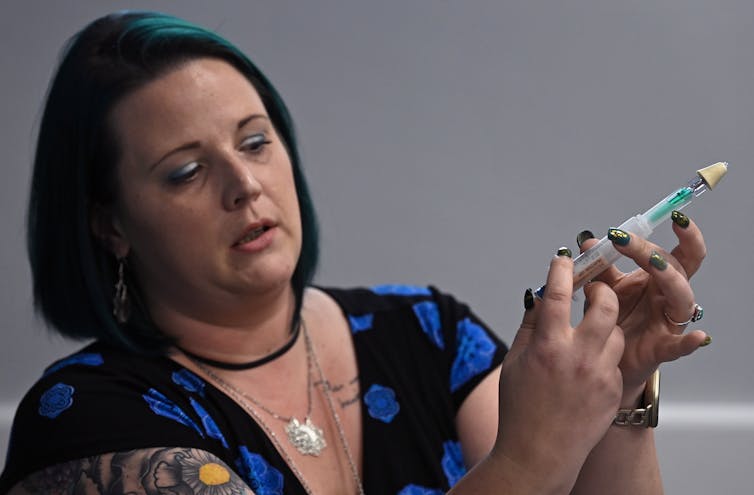 A woman in a blue shirt holds up a clear tube in a demonstration.