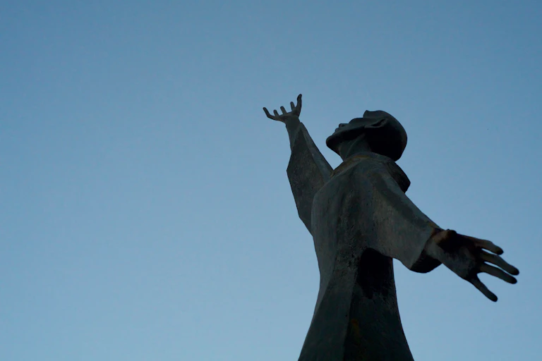 A statue of St Francis of Assisi silhoutted against a bright blue sky in Rome.