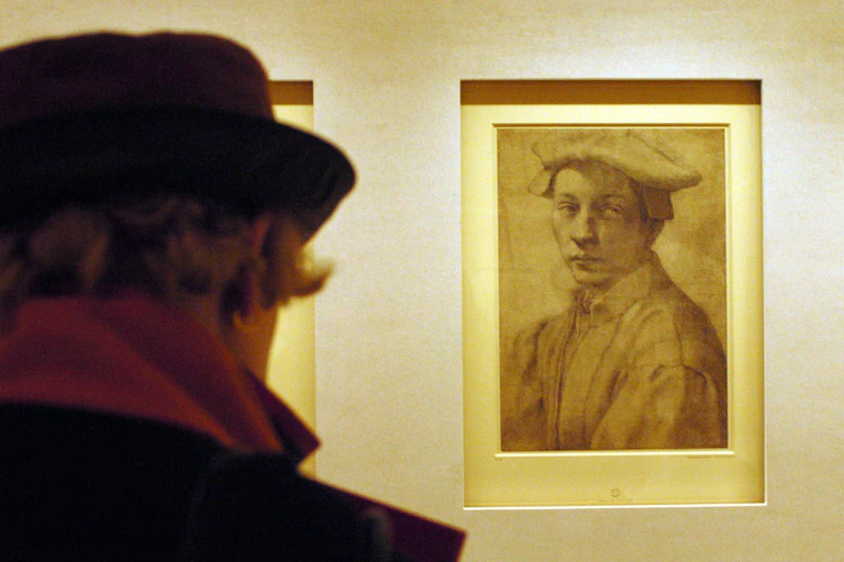A woman in a museum gallery views of sketched portrait of a young man wearing a hat.