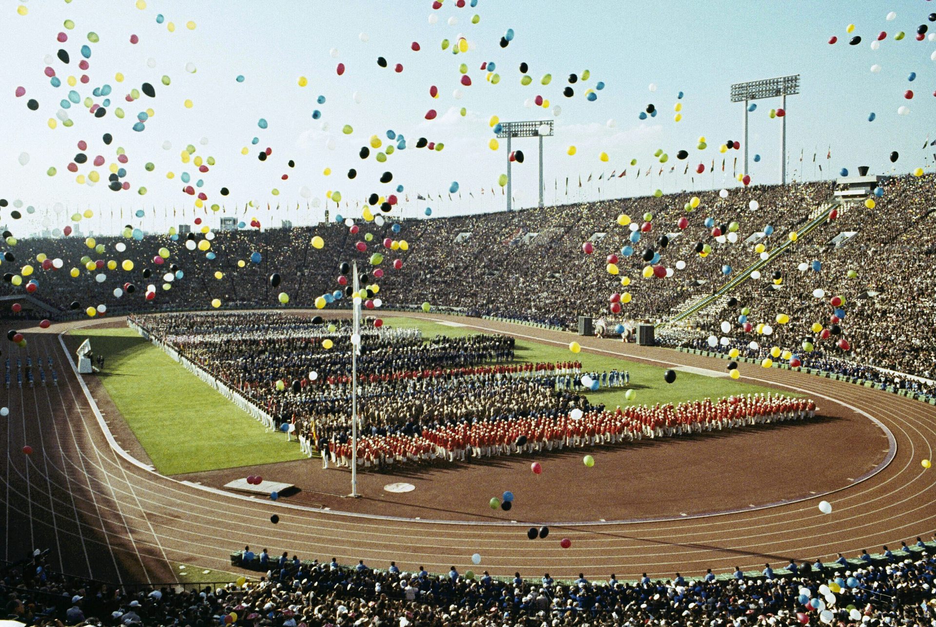 Balloons fly in the air over a track and field venue filled with performers