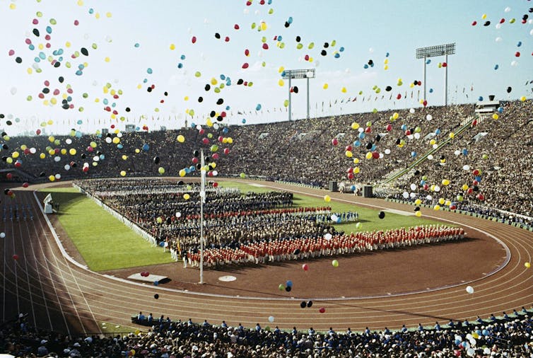 Balloons fly in the air over a track and field venue filled with performers
