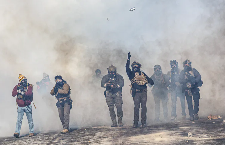 A man dressed in military gear throws a tear gas canister in the air.