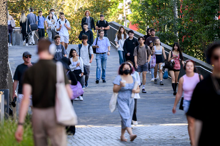 Students walk across a foot bridge on a university campus.