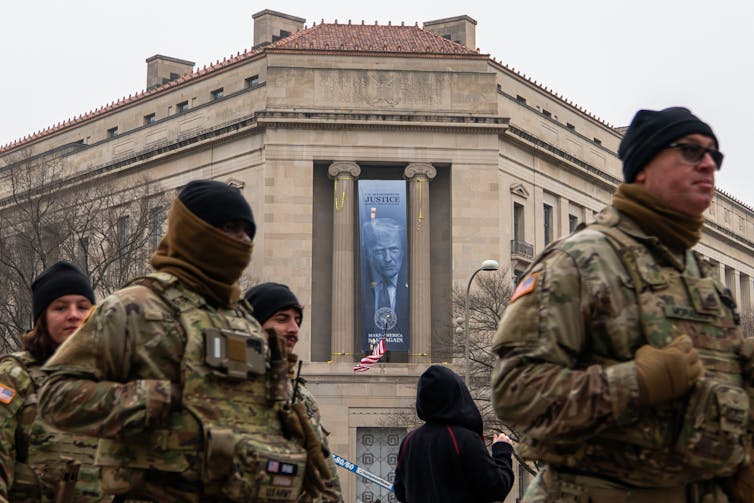 Members of the National Guard walk past a banner with President Donald Trump hanging on the Department of Justice