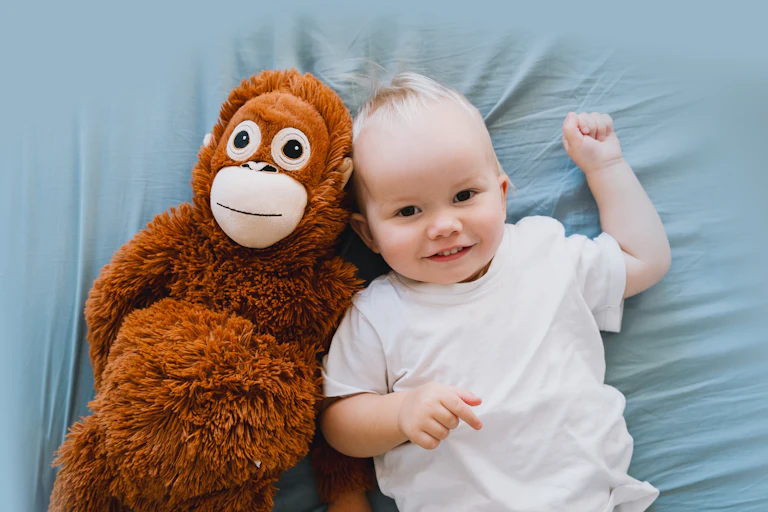 Balita sedang berbaring di tempat tidur di samping boneka monyet