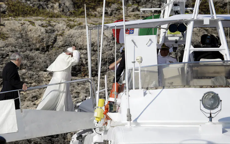 El Papa Francisco, vestido con túnica papal blanca, camina hacia un pequeño barco.