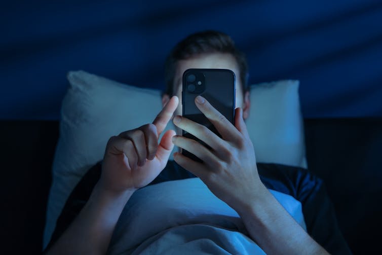 A young man in bed, staring at his phone.