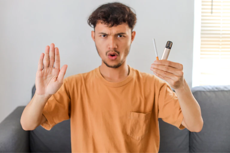 Man holds cigarette and vape in one hand while holding up the other hand in a 'stop' sign
