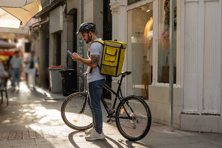 Repartidor mirando un móvil con su bicicleta estacionada