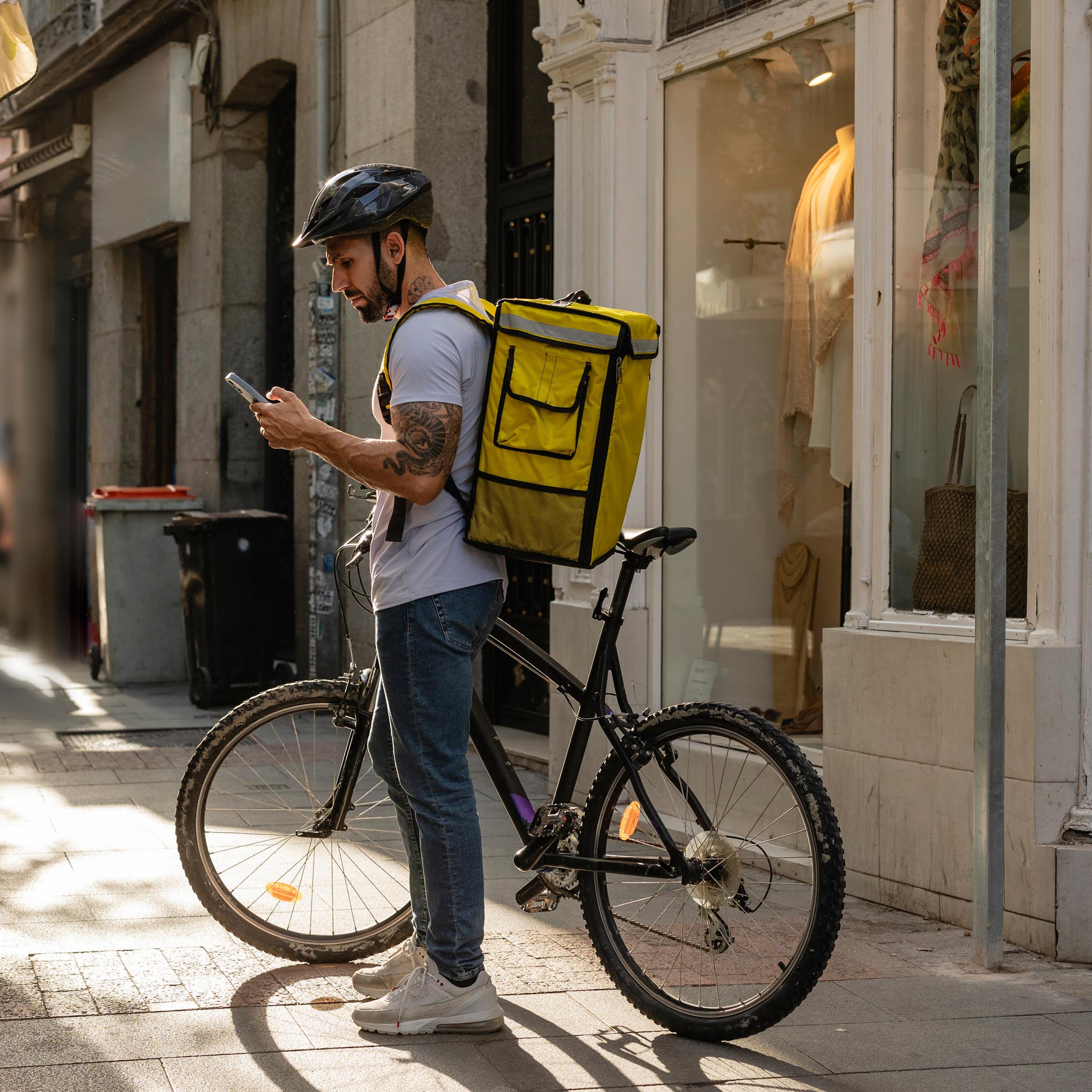 Repartidor mirando un móvil con su bicicleta estacionada