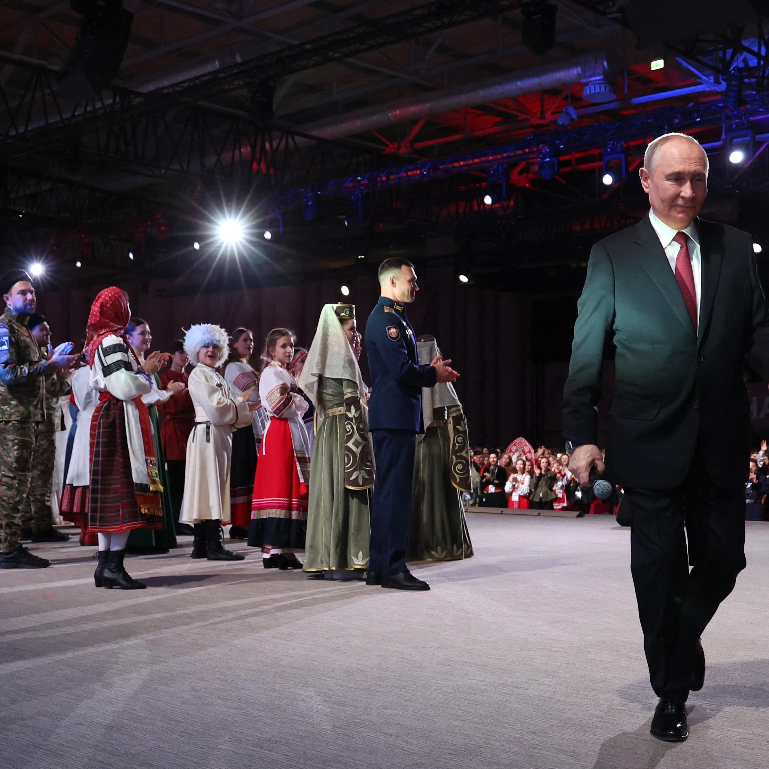 A group of people in traditional Russian garb stand behind a man in a suit