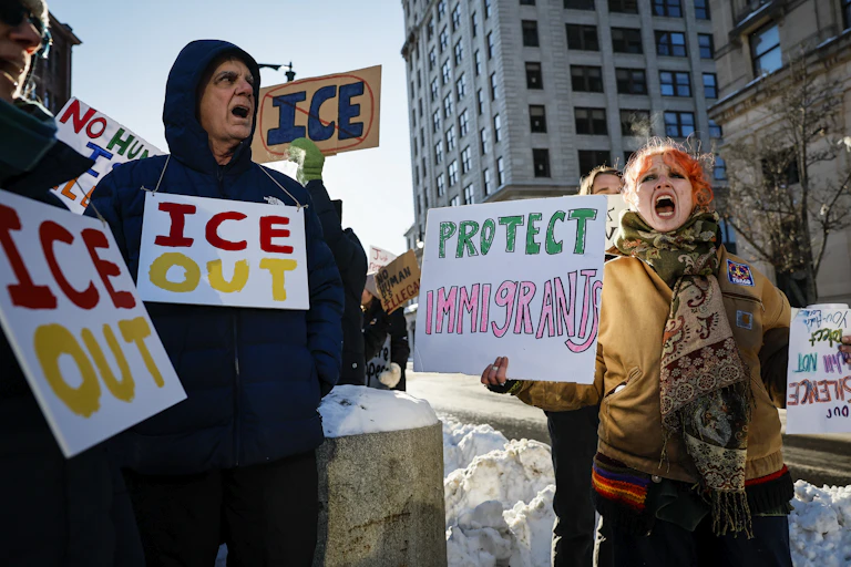 Protesters on a street with signs saying 'ICE OUT' and 'PROTECT Immigrants.'