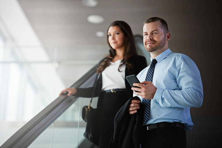 man and a woman in office wear coming down an escalator.