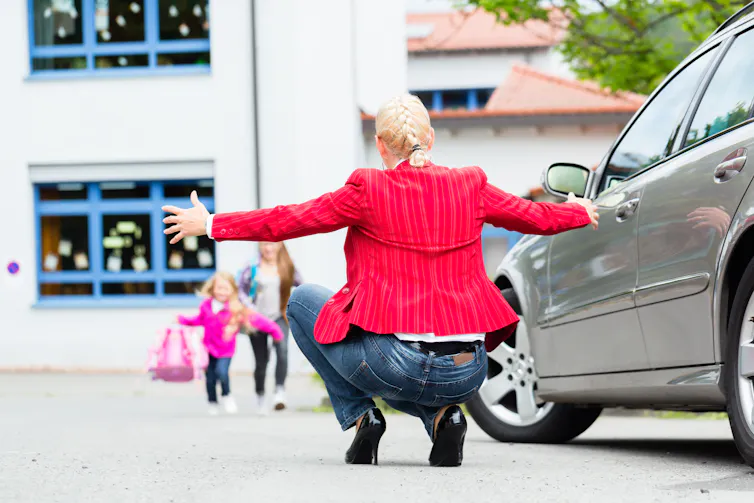 a woman crouches down to greet two children coming out of school.