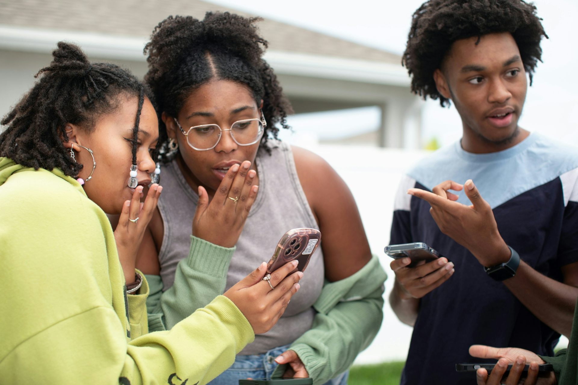 Three Black people holding their phones and discussing.