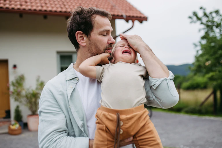 A bearded man seems to speak gently as he holds an upset, angry-looking toddler.
