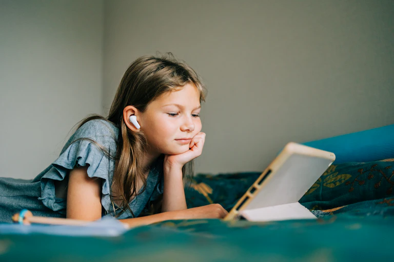 a girl wearing wireless earbuds looks at a tablet screen