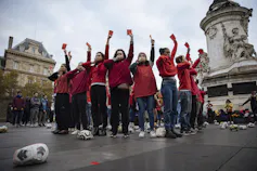 A group of people in red shirts stand in a circle covering their mouths and holding up red soccer cards