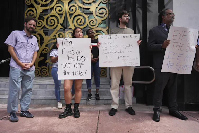 Activists holding signs, including one reading in Spanish, 'FIFA, the world is watching! No masked ICE agents at the games. ICE out of the games, leave us alone.'
