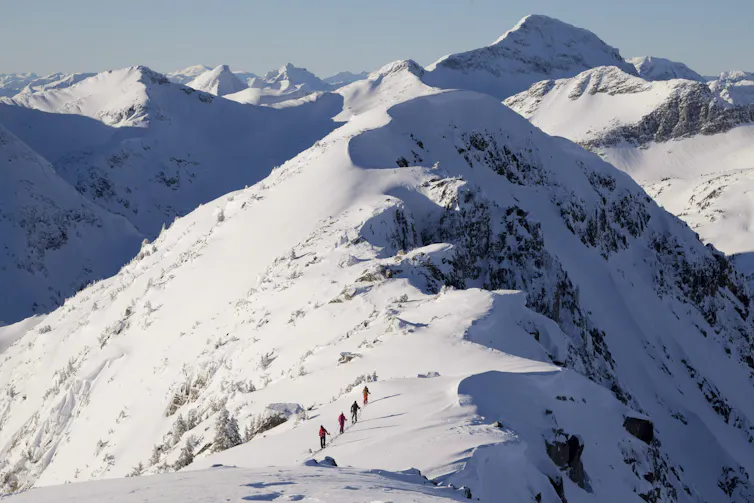 people move across a snow covered area in a mountain range.