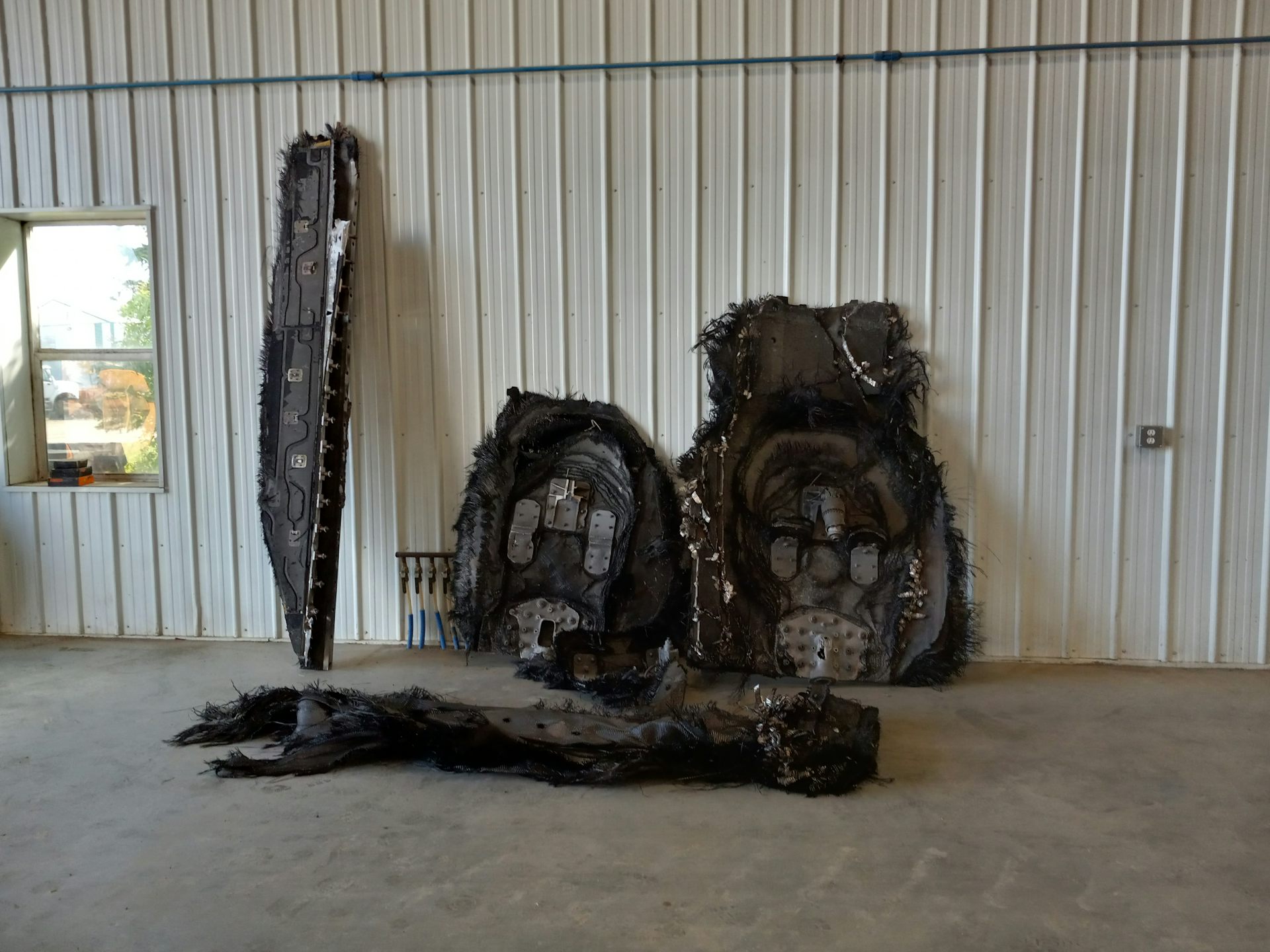 Five person-sized pieces of shredded space debris, leaning on a wall inside a metal-sided building.