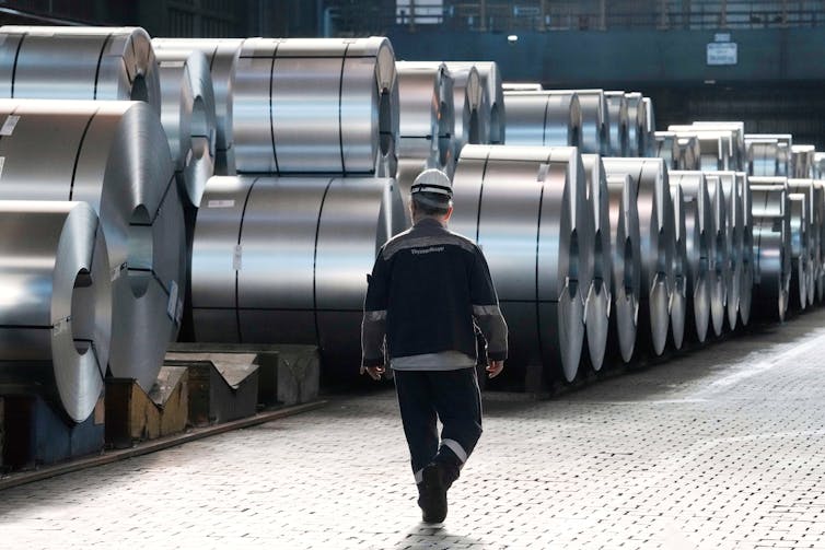 A steel worker walks beside steel coils in a factory