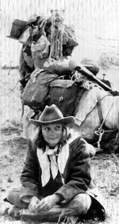 a woman in an Akubra hat with a camel behind her