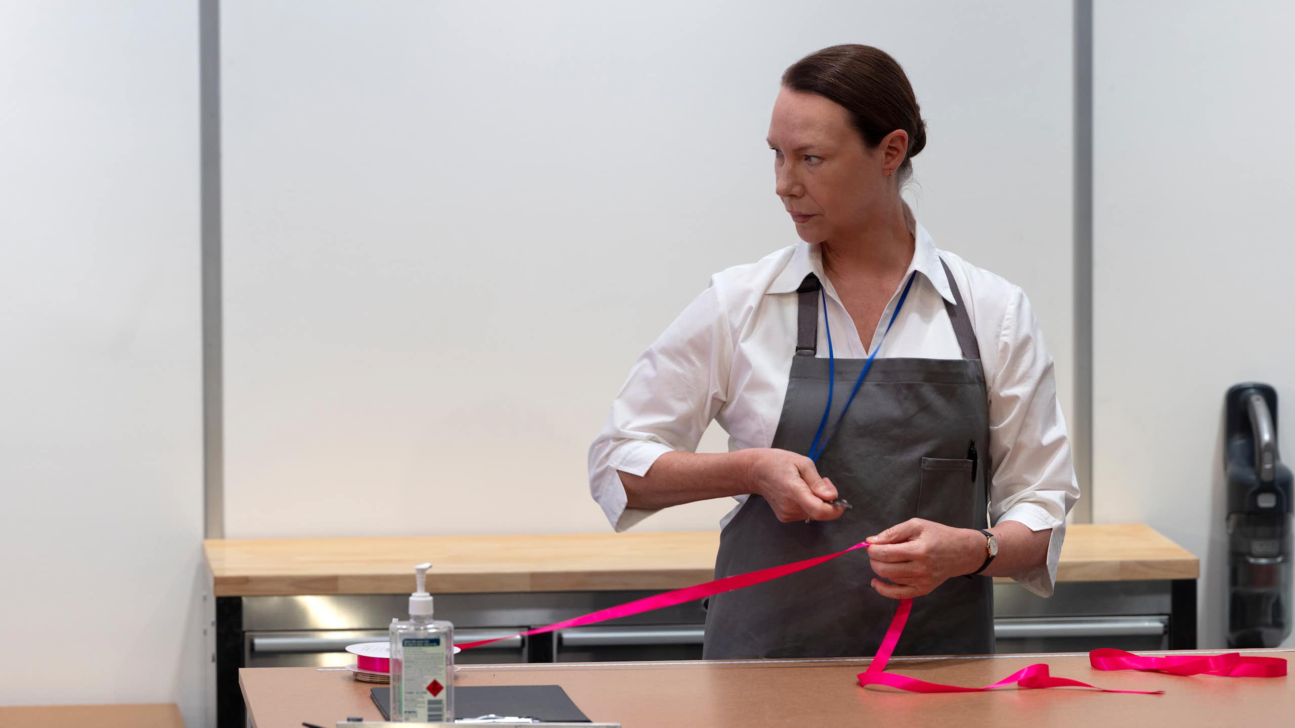 Production image: a woman cuts a ribbon.