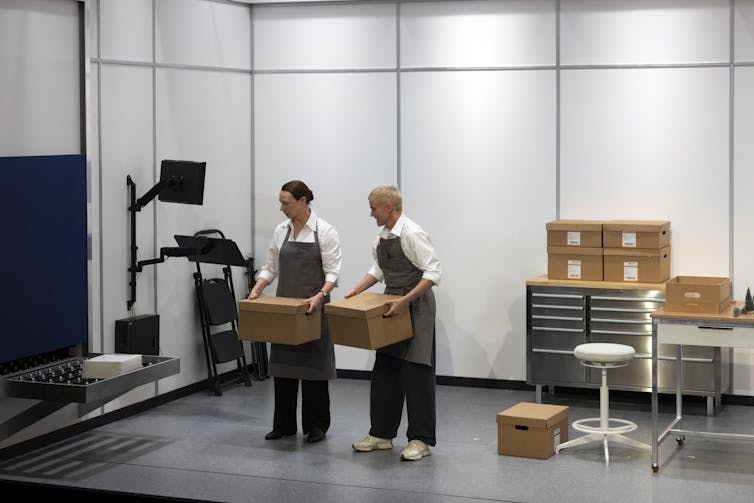 Production image: two people in a sterile room hold boxes and look at where they came from.