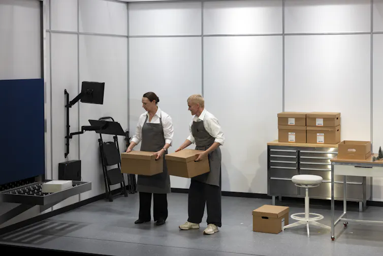 Production image: two people in a sterile room hold boxes and look at where they came from.
