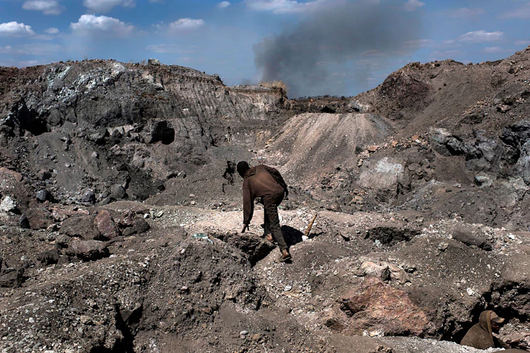 A man in an overall clambering over loose soil and rocks in an open mine
