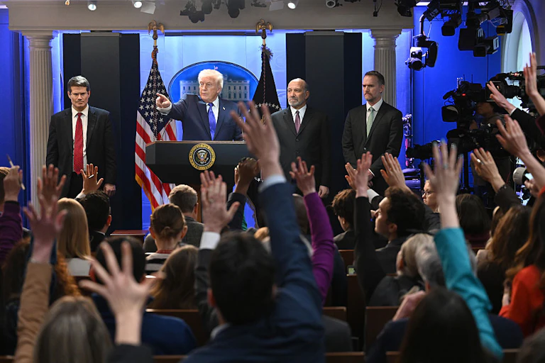 Man at a podium pointing at people seen from behind who have raised hands
