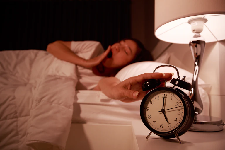 Mujer apagando un despertador que marca las 5 de la mañana