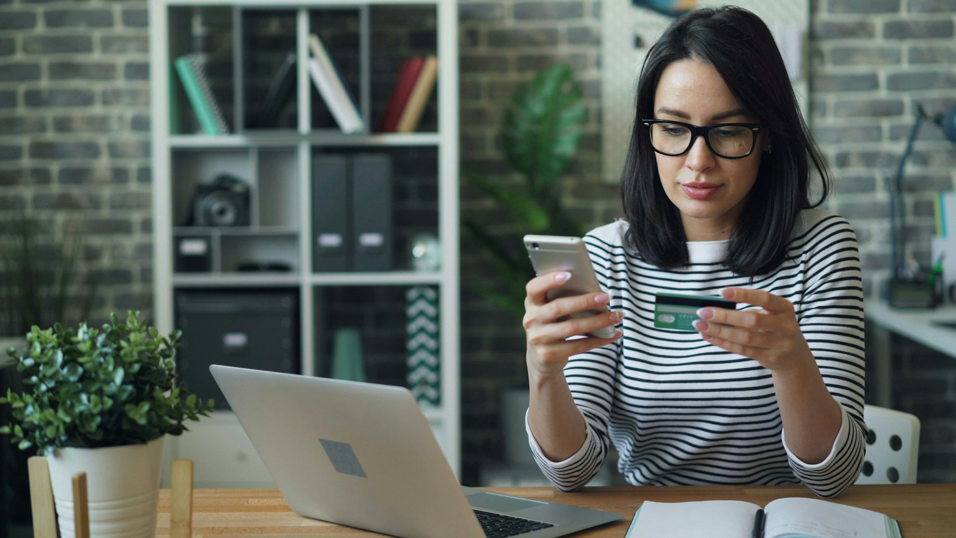A woman looks at her credit card while typing on her cellphone