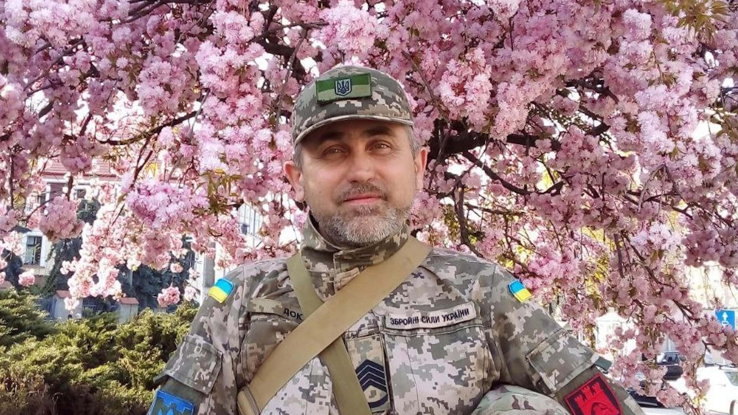 A Ukrainian soldier against a backdrop of pink blossom