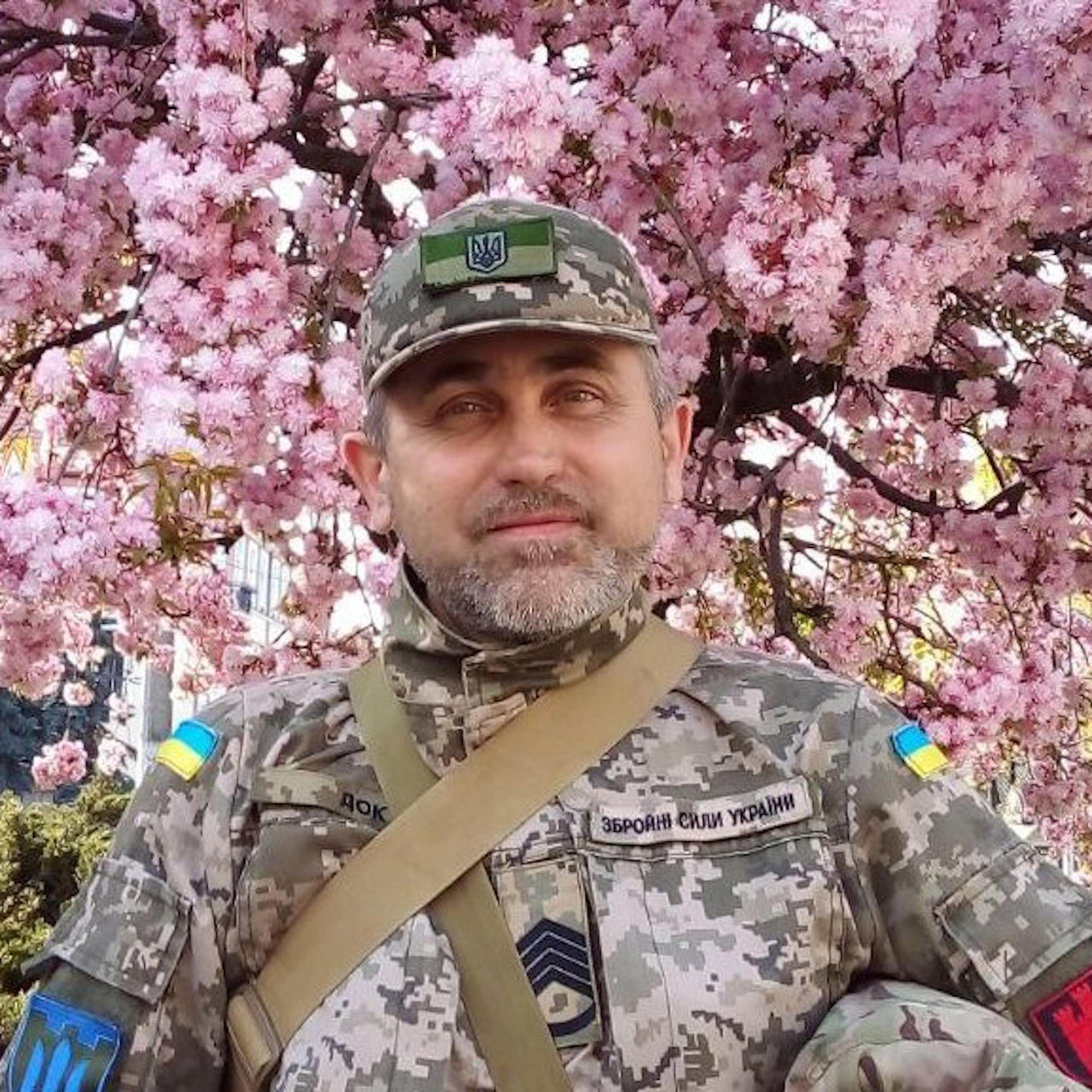 A Ukrainian soldier against a backdrop of pink blossom